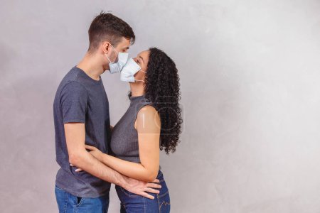 Téléchargez les photos : Les jeunes couples milléniaux portant des masques protecteurs et s'embrassant, la prévention de la propagation du virus et le concept humain. Couple Valentin avec masque. Mise en quarantaine - en image libre de droit