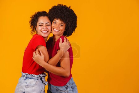 Téléchargez les photos : Afro lesbienne couple sur fond jaune. couple homo-affectif - en image libre de droit