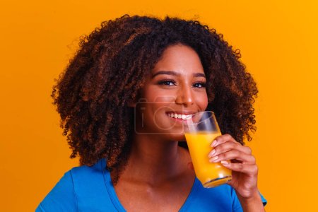 Téléchargez les photos : Femme afro-américaine buvant du jus d'orange en fond jaune - en image libre de droit