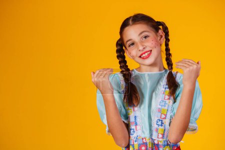 Téléchargez les photos : Enfant en vêtements typiques de la célèbre fête brésilienne appelée Festa Junina pour célébrer So Joo. Belle fille sur fond jaune. - en image libre de droit