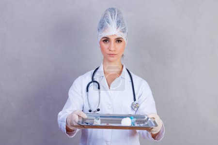 Foto de Enfermera sosteniendo bandeja con medicinas sobre fondo gris. Médicos sobre fondo gris. Vacuna y medicamentos. Concepto de salud y atención - Imagen libre de derechos