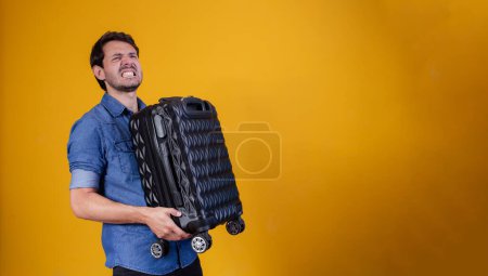 Téléchargez les photos : Homme drôle tenant un sac de voyage lourd. Sur fond jaune - en image libre de droit