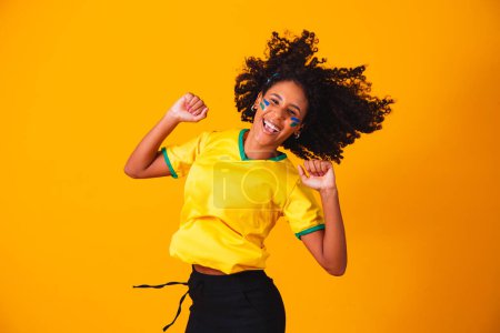 Photo for Brazilian fan. Jumping to celebrate, Brazilian fan celebrating football or soccer game on yellow background. Colors of Brazil. - Royalty Free Image