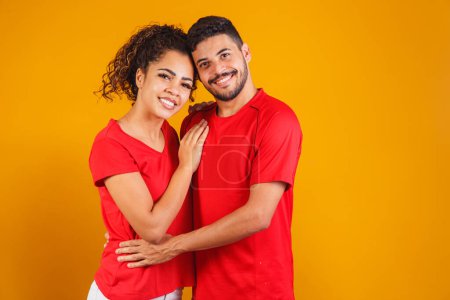 Photo for Portrait of content couple in basic clothing smiling at camera while woman putting her head on male shoulder isolated over yellow background he is surprised and happy - Royalty Free Image