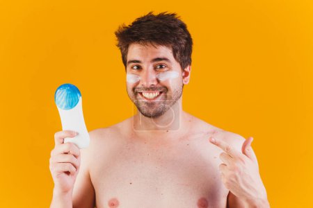 Téléchargez les photos : Beau homme avec barbe en vacances portant des maillots de bain tenant bouteille de lotion solaire regardant positif et heureux debout et souriant avec un sourire confiant montrant les dents - en image libre de droit