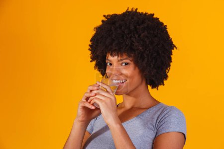 Foto de Joven mujer negra bebiendo agua en fondo amarillo. Chica joven con vaso de agua - Imagen libre de derechos