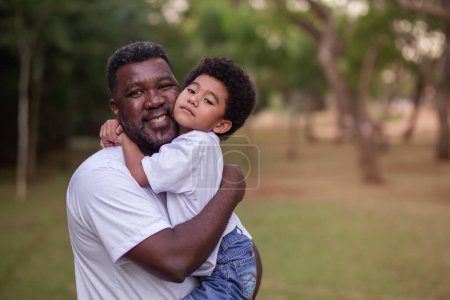 Foto de Padre e hijo afro abrazándose en el parque. Día del Padre. - Imagen libre de derechos