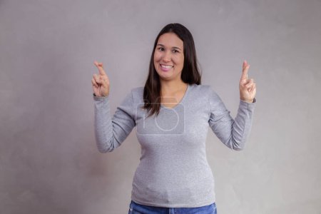 Photo for Asian woman with crossed fingers vibrating victory on gray background. - Royalty Free Image