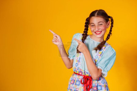 Photo for Child in typical clothes of famous Brazilian party called "Festa Junina" in celebration of So Joo. Beautiful girl on yellow background. - Royalty Free Image