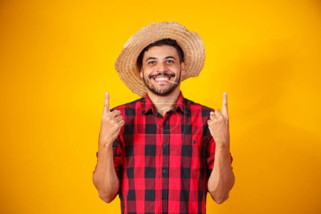 Téléchargez les photos : Homme brésilien portant des vêtements typiques pour la Festa Junina pointant vers le côté avec de l'espace pour le texte - en image libre de droit