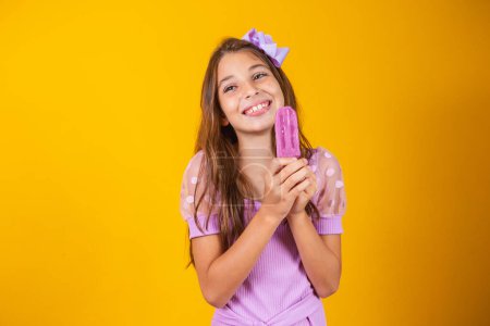 Foto de Pequeña chica caucásica con deliciosa paleta de uva sonriendo mirando a la cámara. Verano - Imagen libre de derechos