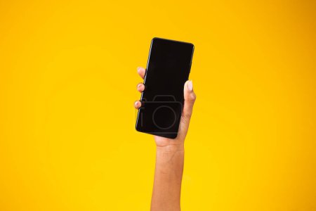 Photo for Hand holding black smartphone isolated on yellow background - Royalty Free Image