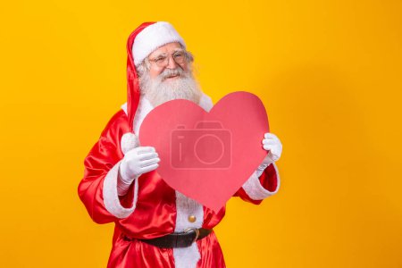 Téléchargez les photos : Père Noël tenant grand carton rouge coeur en arrière-plan jaune. Père Noël romantique. - en image libre de droit