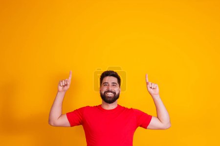 Téléchargez les photos : Bel homme avec barbe pointant vers le haut sur l'espace libre pour le texte sur fond jaune. - en image libre de droit