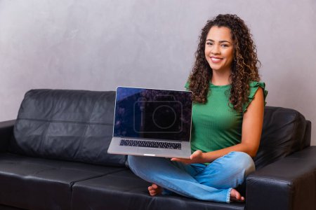 Téléchargez les photos : Jeune femme assise sur le canapé tenant ordinateur portable PC ordinateur avec écran vide avec espace pour le texte. - en image libre de droit