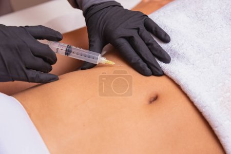 Photo for Cosmetic injection in the spa salon. Beautician makes injection into the patient's belly. the concept of rejuvenation. - Royalty Free Image