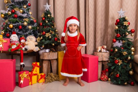 Foto de Linda niña caucásica vestida para Navidad en casa. Chica en fondo de Navidad vestida de noelete - Imagen libre de derechos