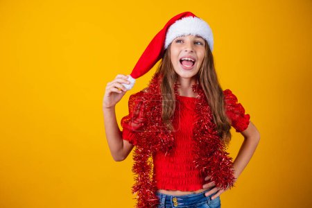 Téléchargez les photos : Petite fille habillée pour Noël enchantée tenant le pompon du chapeau - en image libre de droit