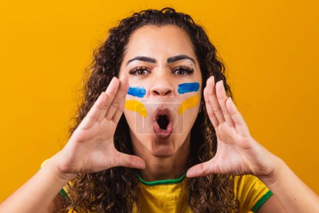 Foto de Abanico brasileño con la cara pintada de azul y amarillo para el juego brasileño. Brasileño celebrando la independencia de Brasil. 7 de septiembre. Abanico brasileño gritando de felicidad - Imagen libre de derechos