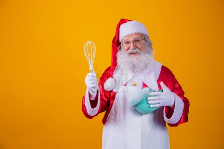 Téléchargez les photos : Père Noël avec un bol battant gâteau sur fond jaune - en image libre de droit