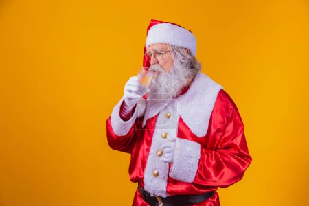 Téléchargez les photos : Père Noël boire un verre d'eau sur fond jaune avec de l'espace pour le texte. Concept santé et hydratation - en image libre de droit
