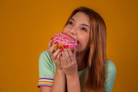 Photo for Girl eating pink donuts on yellow background. - Royalty Free Image