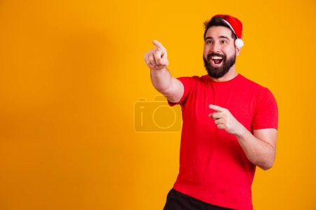 Foto de Hombre guapo vestido para Navidad con sombrero de Santa Claus apuntando a espacio de texto libre. promoción de fin de año - Imagen libre de derechos