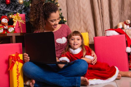 Foto de Familia madre y niña uso de la computadora portátil en casa en vacaciones de Navidad. - Imagen libre de derechos