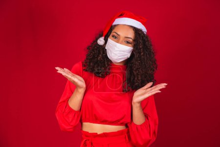 Foto de Joven santa claus mujer en sombrero de Navidad con covid-19 virus coronavirus guardado máscara aislada en el estudio de fondo rojo. Feliz Año Nuevo Celebración Concepto de vacaciones. - Imagen libre de derechos