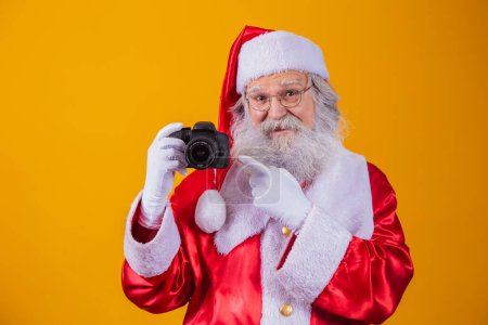 Téléchargez les photos : Père Noël tenant une caméra vintage. Portrait Isolé sur fond jaune
. - en image libre de droit