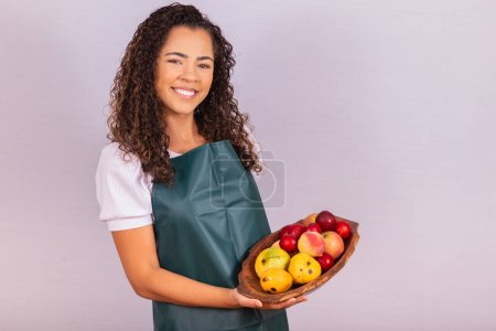Foto de Joven campesina sosteniendo un tazón con frutas. Mango, Melocotón y manzana en la canasta en la mano de la niña - Imagen libre de derechos