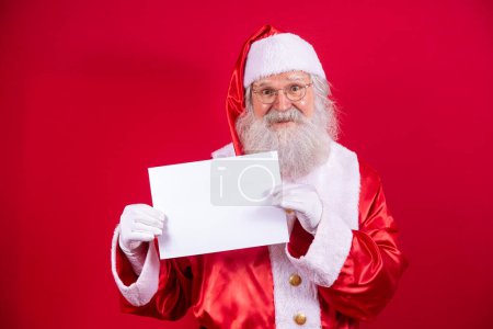 Foto de Feliz Santa Claus sosteniendo un tablero en blanco aislado sobre fondo rojo con espacio de copia. - Imagen libre de derechos