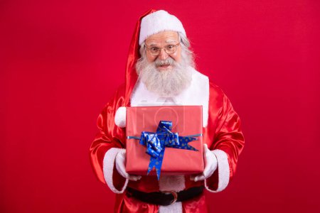 Foto de Santa Claus sosteniendo un regalo de Navidad sobre fondo rojo. - Imagen libre de derechos