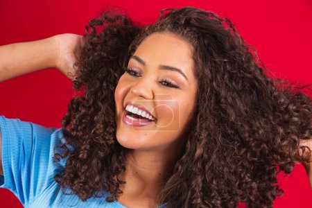 Téléchargez les photos : Portrait de beauté de femme afro-américaine avec coiffure afro et maquillage glamour. Une Brésilienne. Mixte. Cheveux bouclés. Style de cheveuxFond rouge. - en image libre de droit