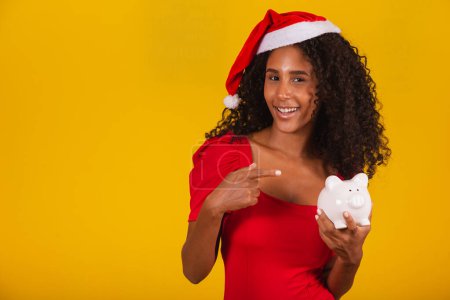 Foto de Hermosa joven que toma los ahorros de una alcancía para comprar los regalos de Navidad. Mujer joven con una alcancía - Imagen libre de derechos