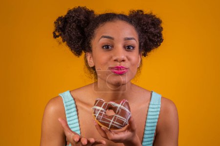Foto de Mujer afro joven comiendo deliciosas rosquillas de chocolate. - Imagen libre de derechos