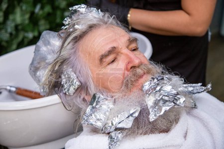 Foto de Papá Noel en el salón de belleza afeitándose y tiñéndose el pelo. Barbudo y peludo senior en el salón de belleza - Imagen libre de derechos