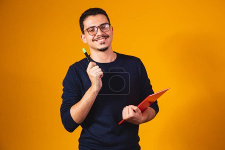 Téléchargez les photos : Portrait de garçon étudiant pensant et tenant un carnet sur fond jaune. - en image libre de droit