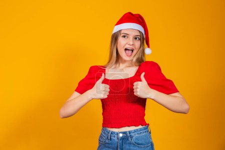 Photo for Portrait of cheerful woman showing thumbs up wearing Santa Claus hat. - Royalty Free Image
