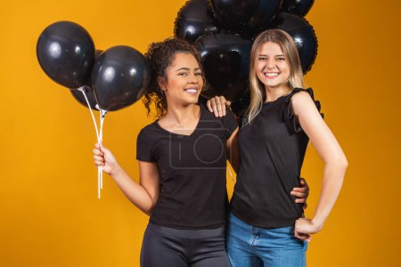 Foto de Dos novias sobre fondo amarillo con globos negros en la fiesta de promoción del viernes negro. - Imagen libre de derechos