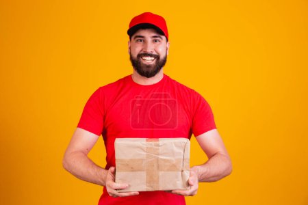 Photo for Best Service Concept. Smiling caucasian delivery man in red cap and stacking holding stack of cardboard boxes while standing isolated over yellow studio background. Mail carrying packages - Royalty Free Image