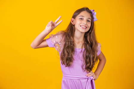 Photo for Photo of a charming and delicate preteen girl making a V sign smiling isolated on yellow background. - Royalty Free Image