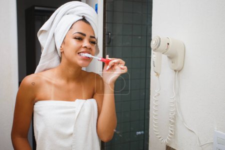 Téléchargez les photos : Afro femme brossant ses dents dans la salle de bain - en image libre de droit