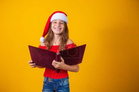 Foto de Hermosa niña caucásica con un libro rojo aterciopelado leyendo historias de Navidad. - Imagen libre de derechos
