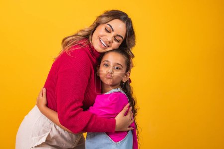 Photo for Photo of a beautiful young mommy holding her arms hugging her little daughter good mood adorable sincere heart feelings in the back jeans t-shirts isolated with yellow color background - Royalty Free Image