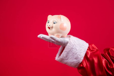 Photo for Close-up of Santa's gloved hand holding a piggy bank. - Royalty Free Image