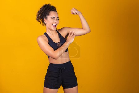 Téléchargez les photos : Image d'une fille afro-américaine forte et confiante, fléchissant ses biceps et le pointant du doigt. - en image libre de droit