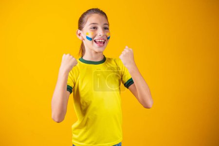 Photo for Beautiful little girl rooting for her team on yellow background. Little girl celebrating the goal and celebrating Brazil's victory - Royalty Free Image