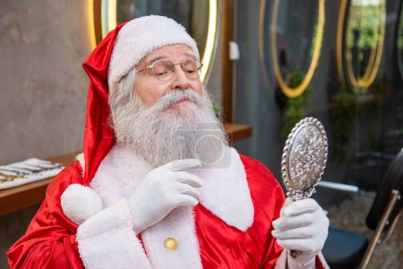 Foto de Real Santa Claus en la barbería sosteniendo un espejo mirándose a sí mismo. - Imagen libre de derechos