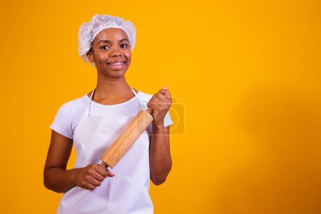 Photo for Young girl pizza maker on yellow background holding rolling pin. - Royalty Free Image